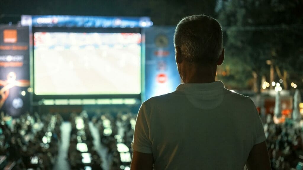 sitting man watching football public place night